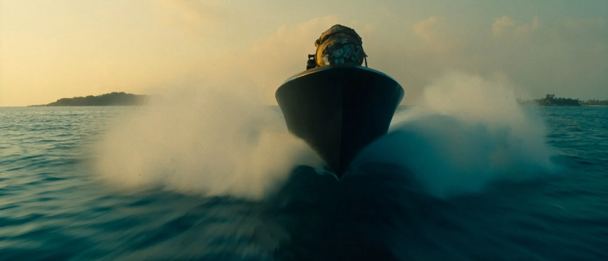 A go-fast boat running at speed at dawn, cargo lashed to the bow, low islands on the horizon.